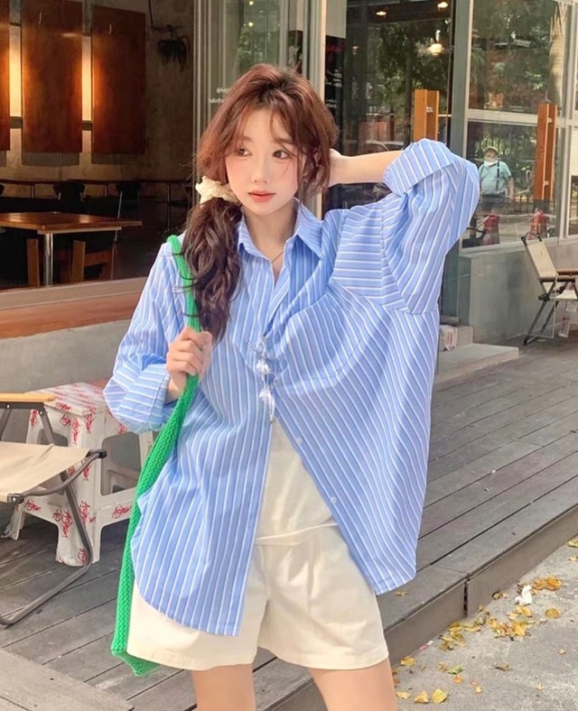 Chiếc sơ mi oversized kẻ sọc xanh trắng kết hợp quần short trắng mang lại vẻ ngoài trẻ trung, thoải mái.