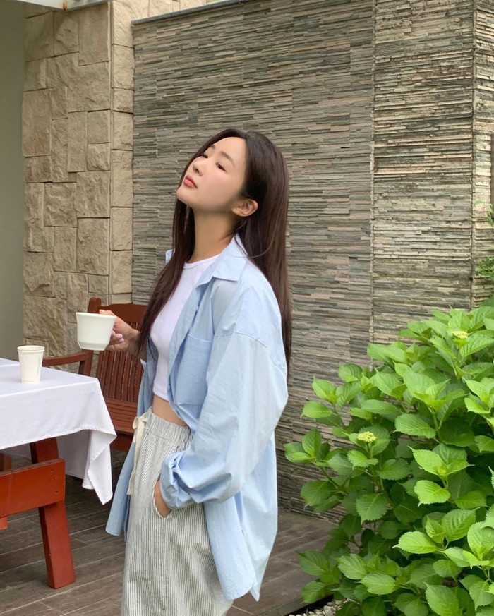 Phối đồ layer mùa hè với áo sơ mi xanh pastel dáng rộng khoác ngoài áo croptop trắng. Quần short sọc đứng tạo cảm giác thoải mái, mát mẻ.