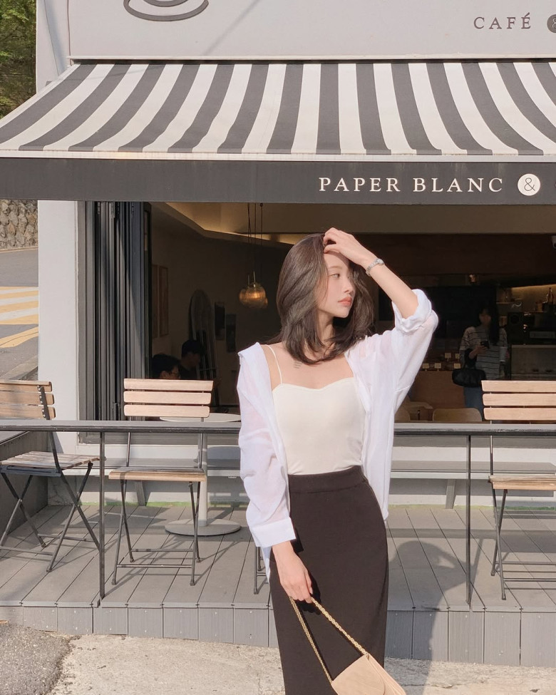 Chiếc áo hai dây lụa mỏng manh cùng sơ mi voan trắng tạo nên lớp layering mềm mại, gợi cảm vừa đủ, tôn lên vẻ đẹp thanh lịch giữa nắng chiều quán cà phê.
