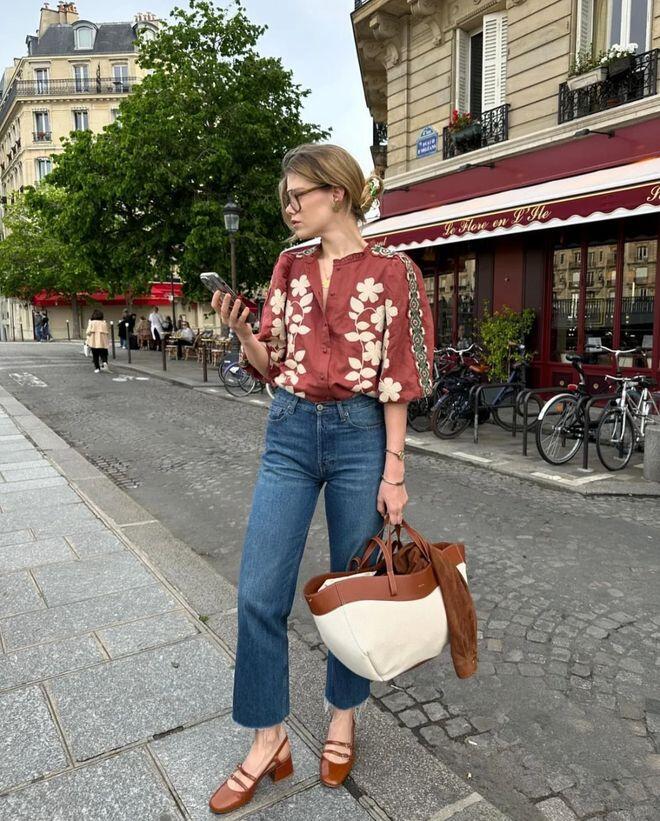Sự tương phản ngọt ngào giữa áo sơ mi đỏ đô thêu hoa trắng nổi bật và quần jeans ống đứng mang đến vẻ ngoài vừa cổ điển, vừa hiện đại.