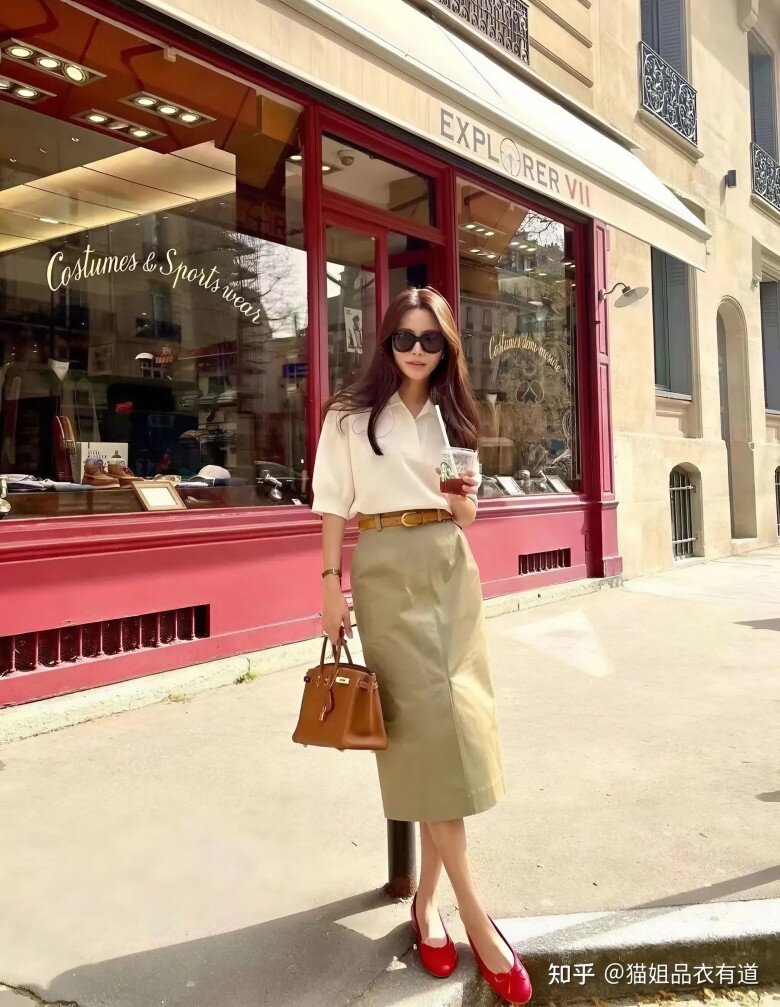 Sự quyến rũ cổ điển lan tỏa qua áo polo trắng và váy midi kaki thanh thoát, điểm xuyết đôi giày đỏ rực rỡ.