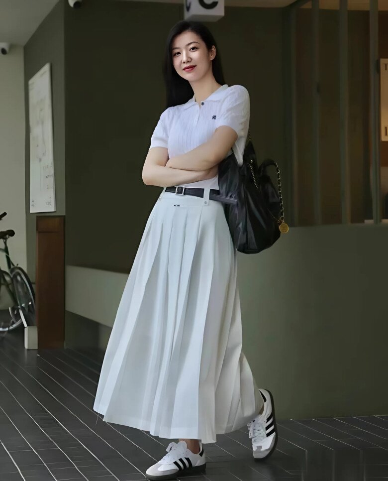 Vẻ đẹp phóng khoáng nhẹ nhàng với áo polo trắng và váy xếp ly dài, hòa quyện cùng giày Adidas năng động.