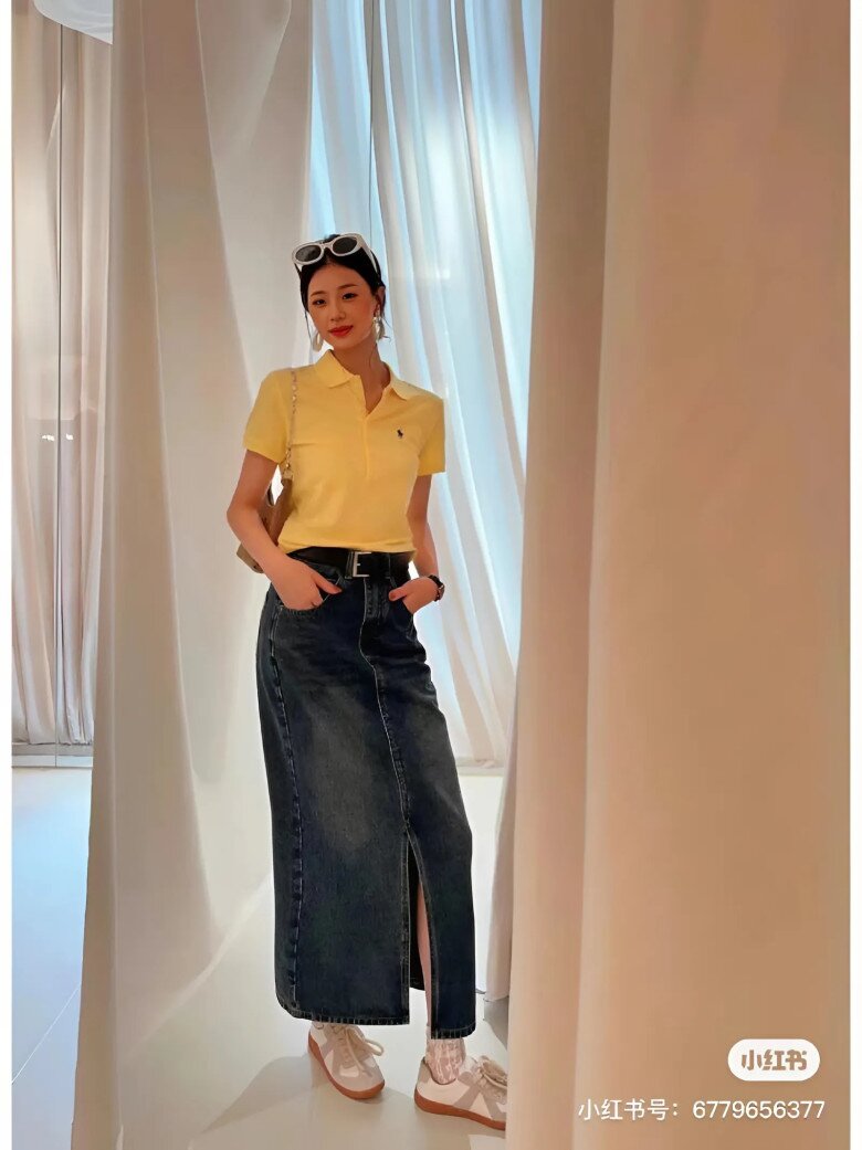 Tông vàng pastel từ áo polo nổi bật trên nền chân váy denim dài xẻ trước, tạo nên tổng thể retro pha chút thể thao.