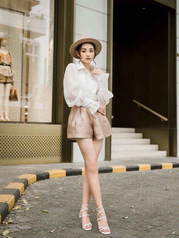Thanh lịch và thời thượng, quần short lụa chữ A phối cùng áo blouse tay bồng trắng tạo nên tổng thể nhẹ nhàng, bay bổng. Giày sandal cao gót buộc dây tôn dáng triệt để, giúp đôi chân thêm dài và thanh thoát.