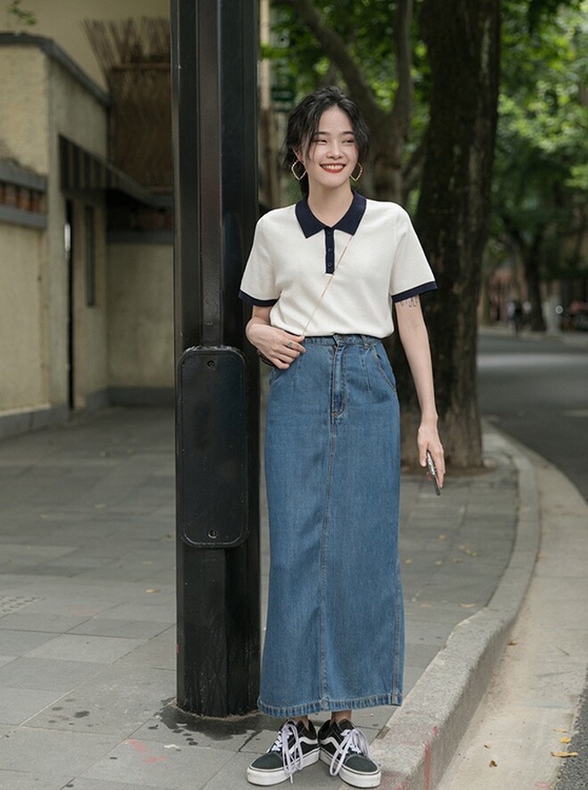Phong cách street style trẻ trung với váy denim dáng ôm dài, kết hợp áo polo tương phản màu sắc. Váy jeans ôm tôn dáng, vừa mang hơi thở retro, vừa hiện đại nhờ vào cách phối giày sneakers khỏe khoắn và nụ cười rạng rỡ.