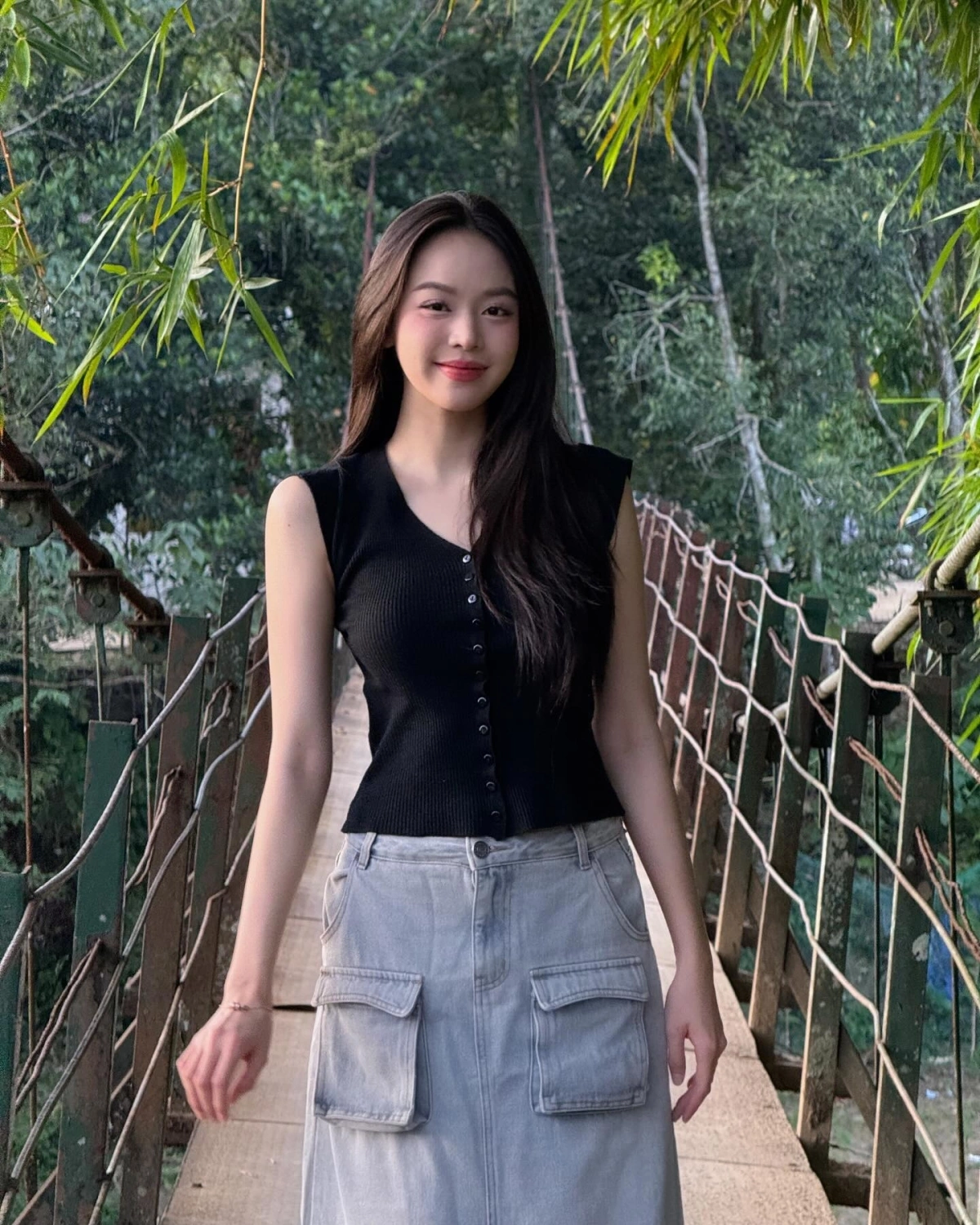 Thanh Thủy diện áo tank top đen ôm sát phối cùng chân váy denim túi hộp màu xám nhạt mang hơi hướng utility hiện đại.