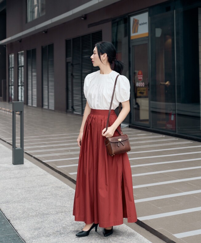 Áo blouse trắng tay bồng đi cùng chân váy maxi đỏ đất thể hiện sự cân bằng giữa cổ điển và thanh lịch.