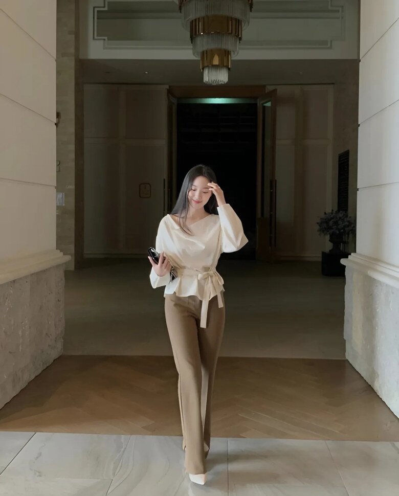 Chiếc áo trắng kiểu peplum thắt nơ tôn vòng eo, kết hợp quần ống suông màu nâu trầm tạo hiệu ứng thanh lịch và sang trọng.