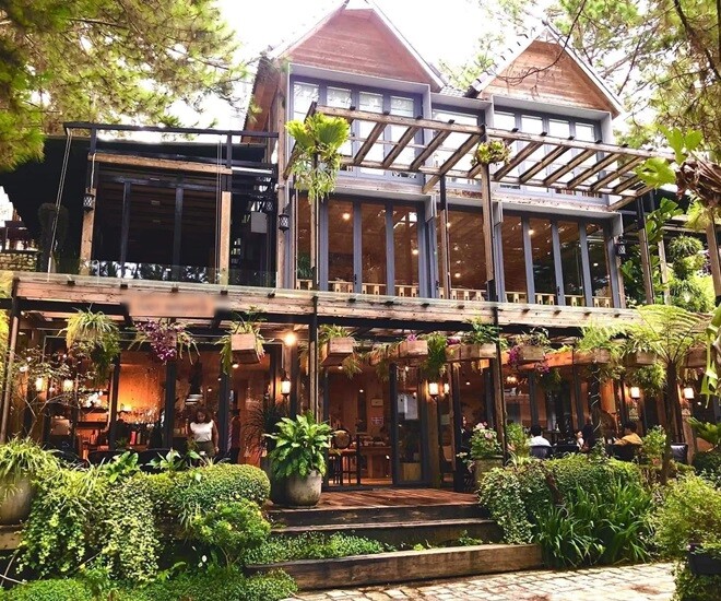 2 căn biệt thự nổi bật của Phan Như Thảo ở Đà Lạt với mái nhọn và khung kính lớn, bao quanh là cây xanh và hoa rực rỡ. Thiết kế kết hợp gỗ thông và kính giúp không gian luôn tràn đầy ánh sáng.