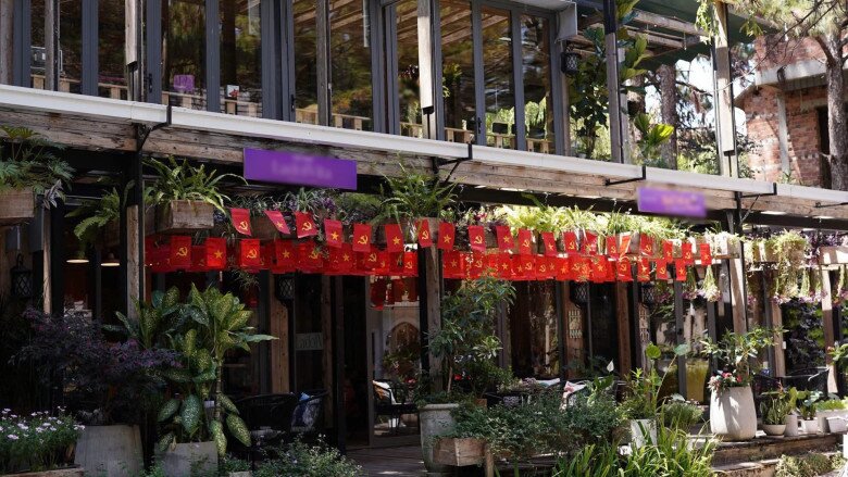 Mặt tiền biệt thự vào dịp lễ với cờ trang trí đỏ rực nổi bật. Bên dưới là hàng cây xanh và giỏ hoa treo tạo nên khung cảnh sống động như một khu phố cổ.