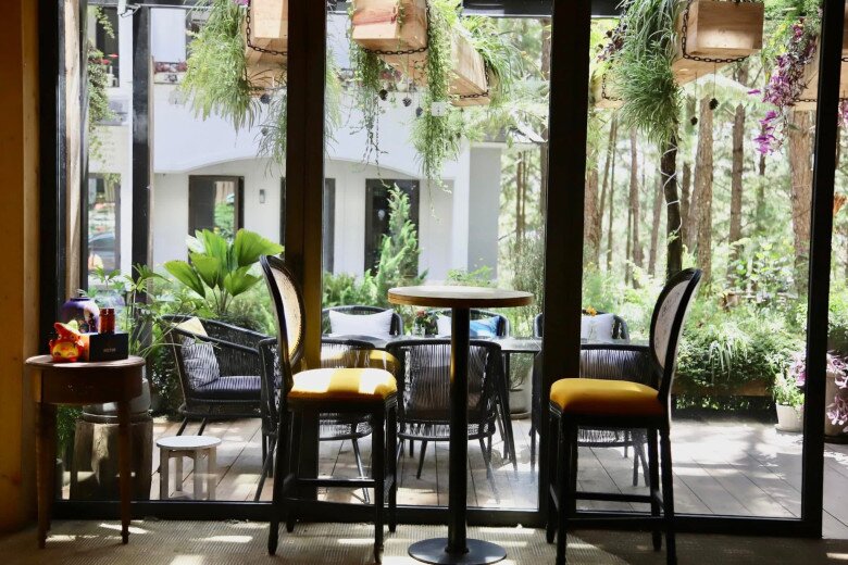 Một góc nhìn ra sân vườn với cửa kính cao, đối diện là bàn tròn và ghế cao. Đây quả là nơi lý tưởng để thưởng thức ly cà phê sáng giữa không gian xanh mướt.