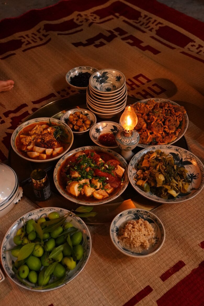 Mâm cơm nhà Linh gồm nhiều món dân dã: Đậu phụ kho cà chua đậm đà, canh cua nấu khoai sọ nóng hổi, cải chua xào giòn giòn, rạm đồng chiên vàng ruộm, dưa xanh chấm muối và một bát cơm nếp dẻo thơm.