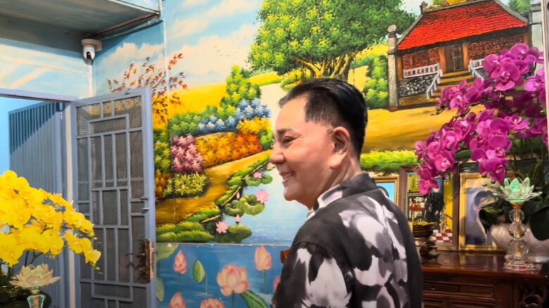 Một bức tường rực rỡ sắc hoa và tranh vẽ. Cảnh vật vẽ tay tạo chiều sâu và cảm giác như đang đứng giữa thiên nhiên. Hoa lan thật cũng tạo điểm nhấn dịu dàng bên cạnh.