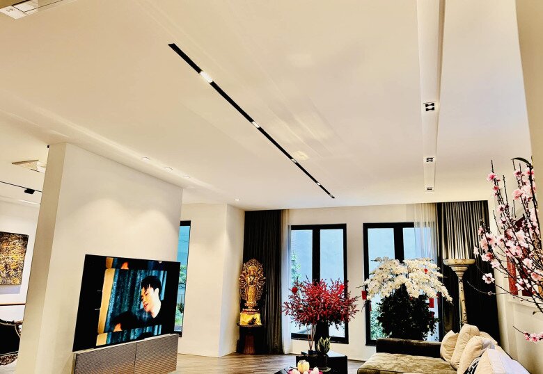 Phòng khách ngập sáng tự nhiên với nhiều loại hoa như đào, lan hồ điệp và mai đỏ được cắm tươi tắn, bố trí dọc theo cửa kính và các góc phòng.
