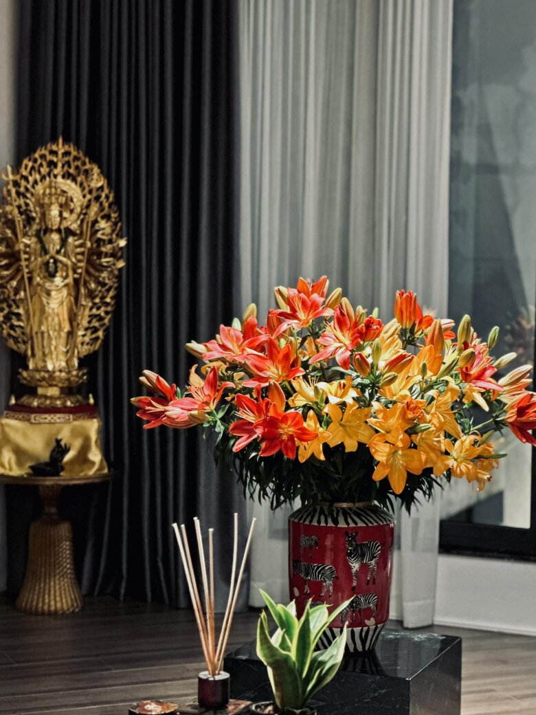 Bình hoa huệ đỏ cam đặt bên tượng Phật nghìn tay, gợi cảm giác trang nghiêm nhưng không kém phần tươi sáng, gần gũi trong góc thờ.