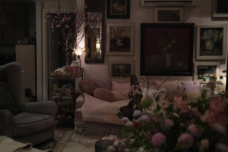 Tường treo kín tranh, chủ yếu là tranh tĩnh vật và phong cảnh, giúp không gian thêm chiều sâu. Bộ sofa vintage với gối và chăn len gợi cảm giác êm ái, thư giãn.