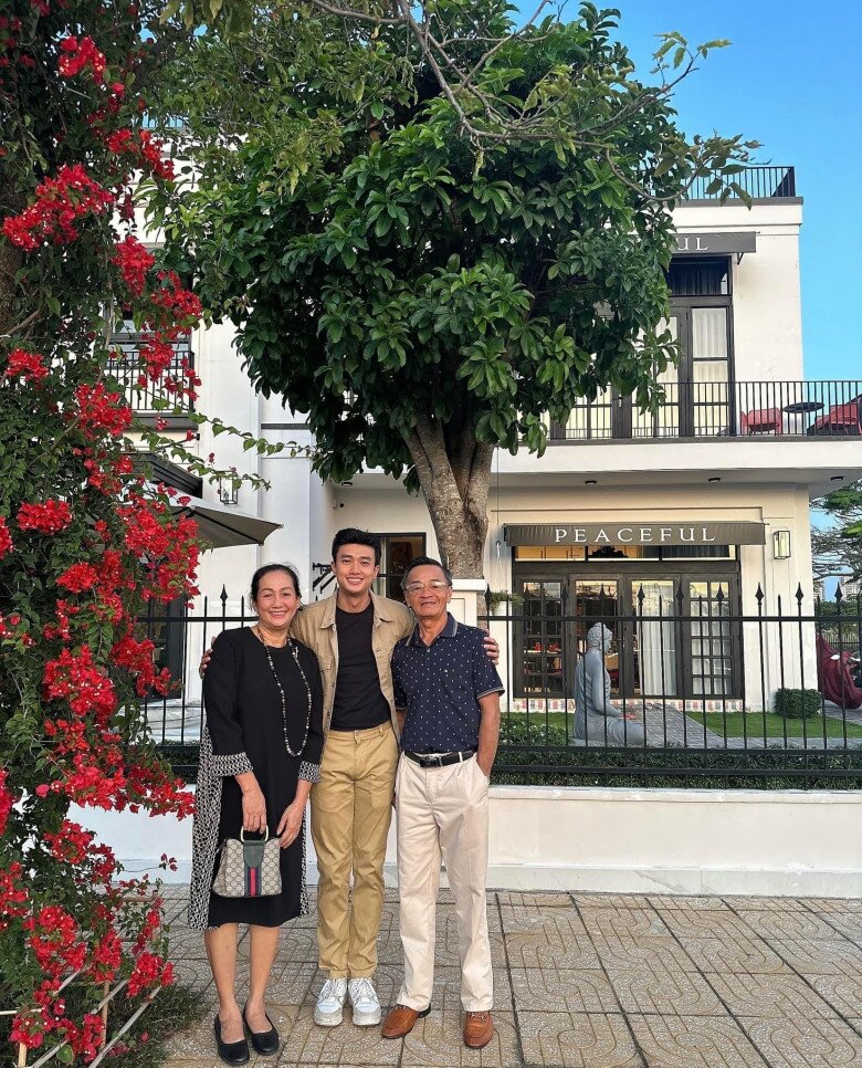 Trong một khoảnh khắc đời thường, Quốc Trường chụp ảnh cùng bố mẹ trước cổng nhà, nơi giàn hoa giấy đỏ tạo điểm nhấn nổi bật trên nền trắng tinh của biệt thự.