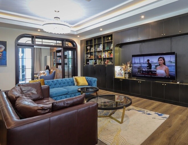 Phòng khách rộng rãi với hai bộ sofa xanh và nâu, bàn trà kính tròn, tận dụng ánh sáng tự nhiên qua hệ cửa kính khung vòm đầy tinh tế.