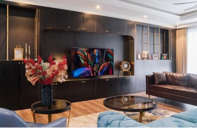 Tầm nhìn từ sofa ra kệ trưng bày, nơi lưu giữ sách, hình ảnh và kỷ vật gia đình, gam màu tối tạo sự sang trọng nhưng gần gũi.