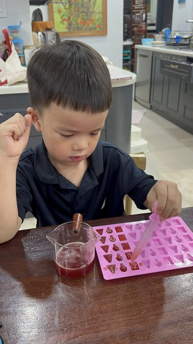 Cậu bé Ruốc tập trung dùng ống nhỏ giọt đổ hỗn hợp vào khuôn silicon. Bàn tay nhỏ nhắn nhưng thao tác đầy kiên nhẫn và khéo léo.