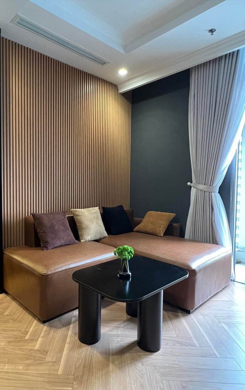 Sofa da nâu trầm, kết hợp với tường lam gỗ và đệm vải nhiều màu tạo nên sự ấm cúng và gần gũi, phù hợp với tính cách nhẹ nhàng của nam nhạc sĩ.