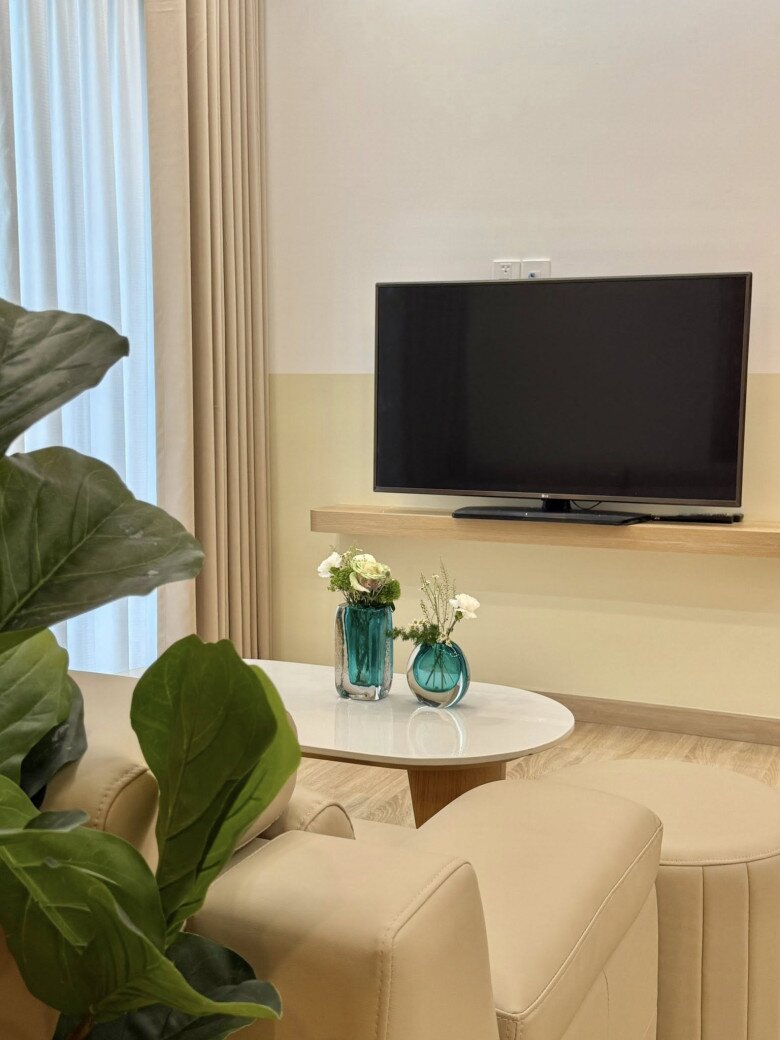 Góc phòng khách sáng sủa với sofa kem, bàn trà tròn và những bình hoa xanh ngọc làm điểm nhấn. Màn cửa hai lớp giúp điều chỉnh ánh sáng theo ý muốn.