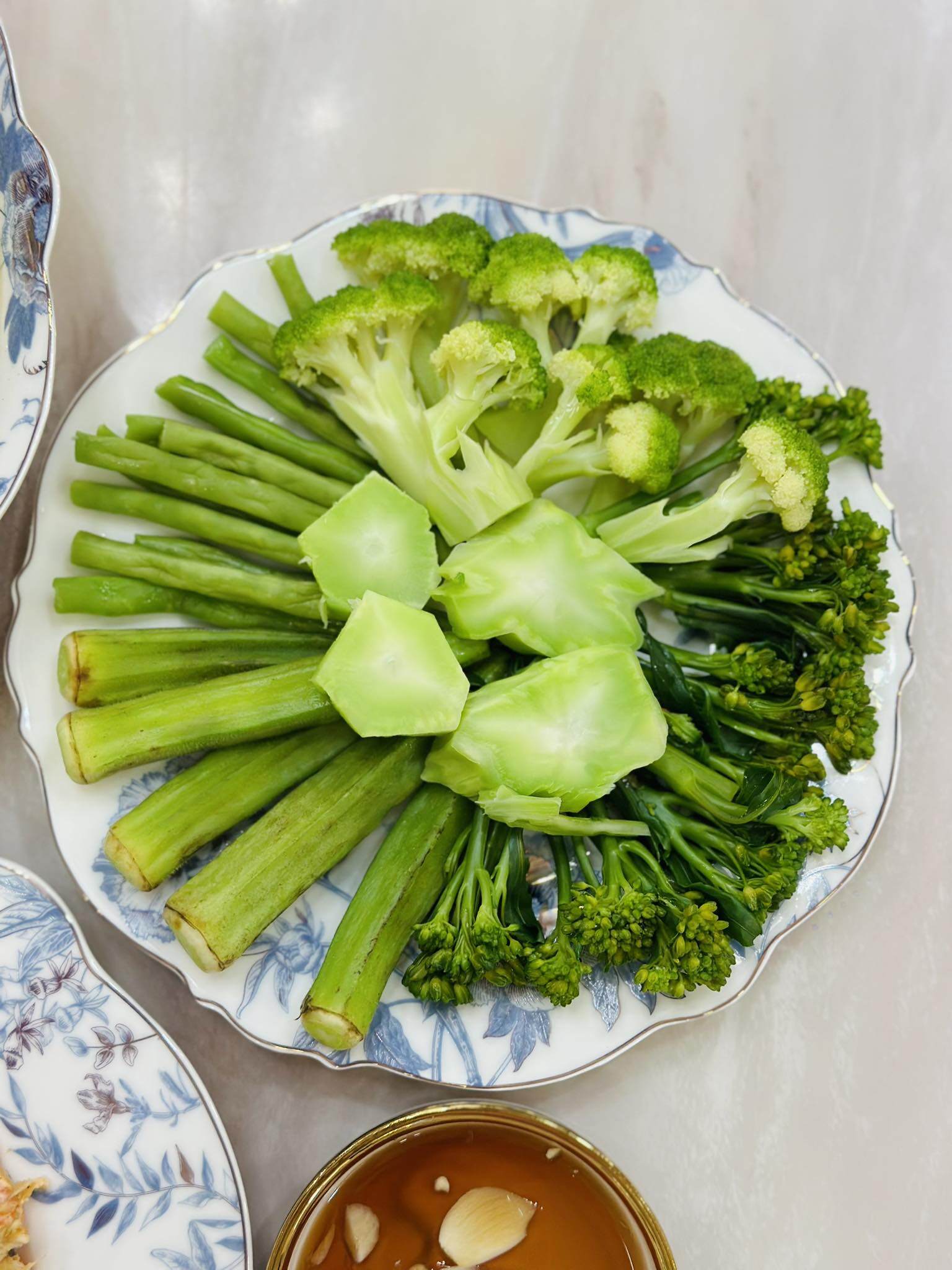 Đĩa rau luộc gồm súp lơ xanh, bông cải và thân bông cải, ăn kèm nước mắm tỏi ớt đậm đà. Một lựa chọn lành mạnh, vừa giúp cân bằng dinh dưỡng vừa làm dịu vị cho cả mâm cơm.