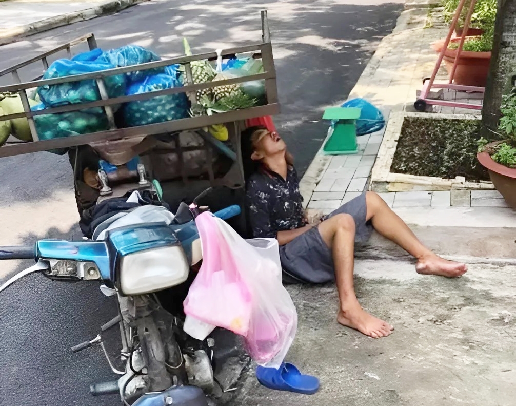 Anh bán hoa quả ngủ gục bên lề đường, tay vẫn cầm xấp tiền lẻ khiến nhiều người xót xa