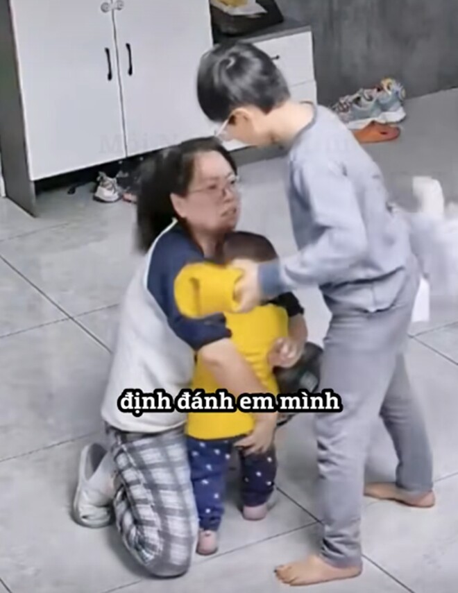 Người anh tức giận muốn đánh em, mẹ ra sức bảo vệ bằng lời nói và hành động.