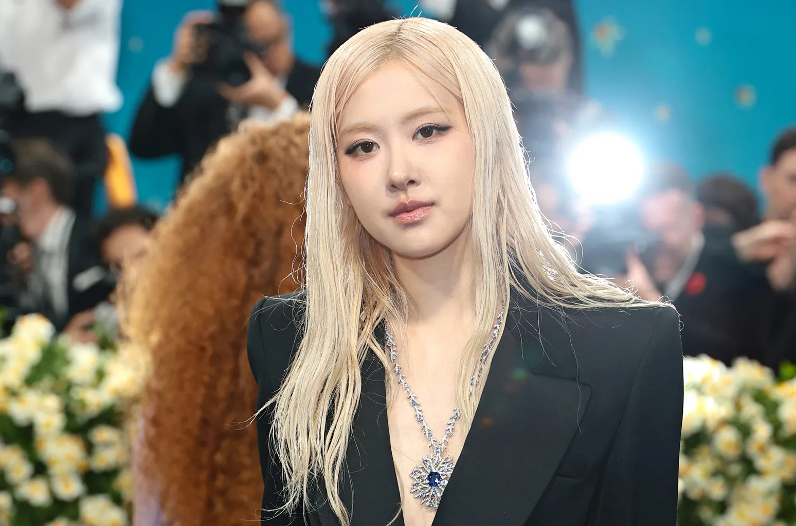 Rosé vẫn giữ phong cách trang điểm đặc trưng của mình, với điểm nhấn là đôi mắt được kẻ eyeliner cánh sắc sảo, kết hợp phấn mắt tông nude nhẹ, tạo ánh nhìn cuốn hút nhưng không quá đậm. Má hồng được đánh nhẹ tông hồng đào, mang lại vẻ tươi tắn, và đôi môi được phủ một lớp son bóng hồng nhạt.