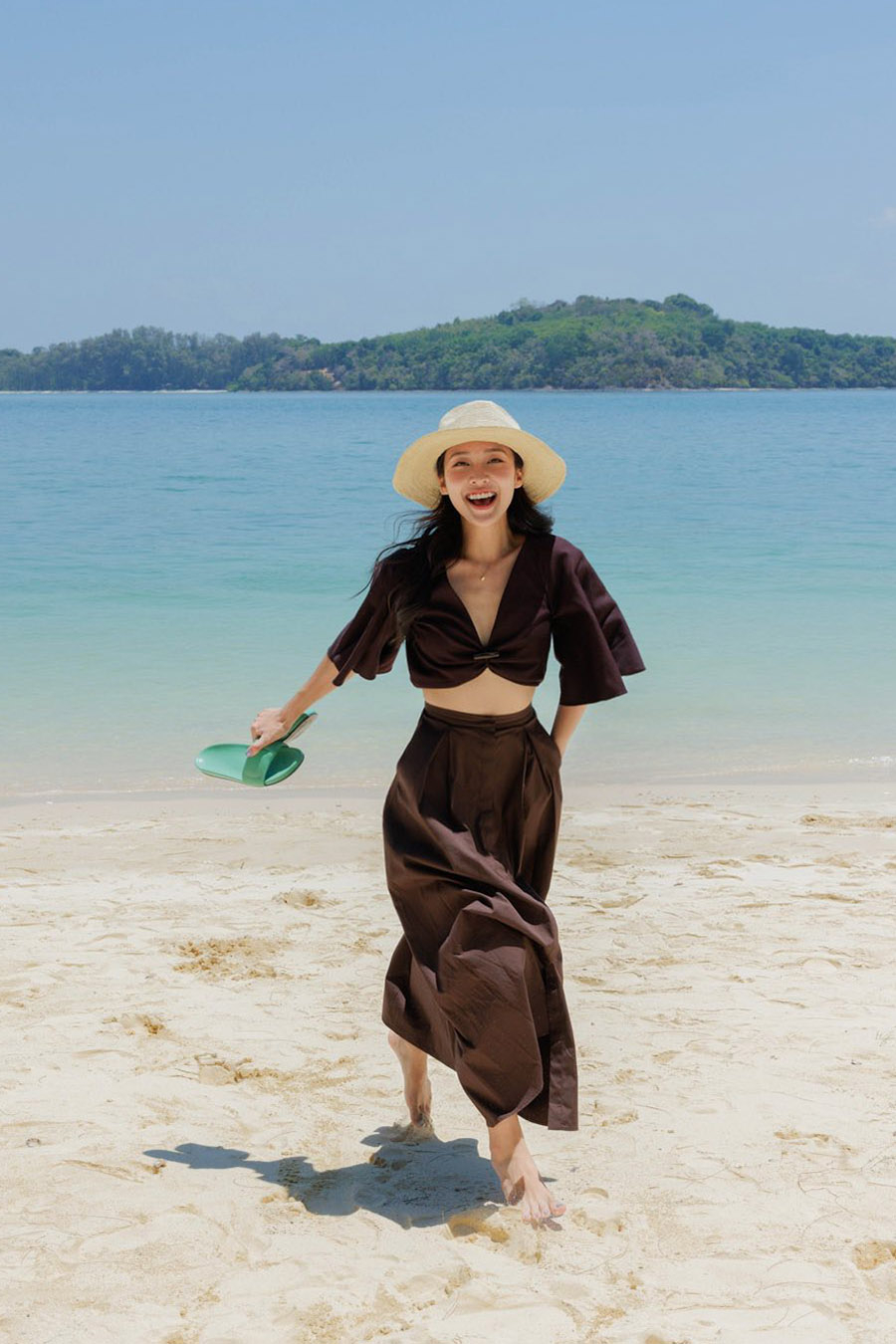 Khả Ngân đang tận hưởng chuyến du lịch Thái Lan cùng ca sĩ Ái Phương và nhóm bạn. Trong ngày dạo chơi tại Phuket, cô tạo điểm nhấn phong cách bằng crop top cài một nút và chân váy maxi đồng điệu.