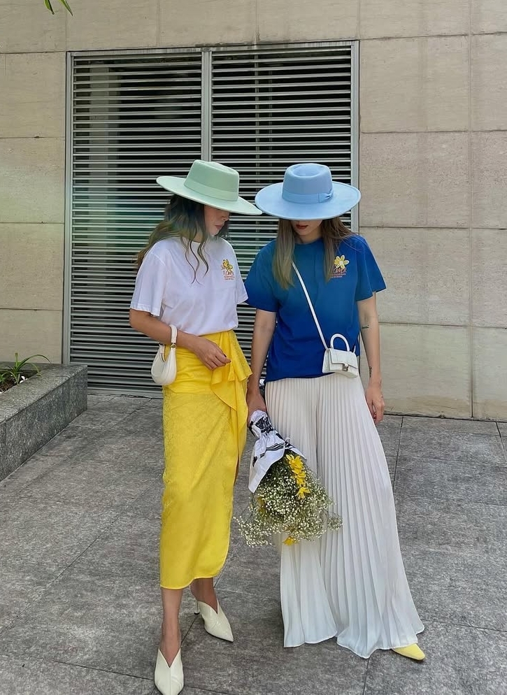 Cùng phối áo phông, chân váy, mũ rộng vành và dép cao gót nhưng cả hai vẫn tạo được nét riêng. Yến Trang chọn chân váy bất đối xứng dáng tulip. Yến Nhi diện váy maxi chữ A dài quét đất.
