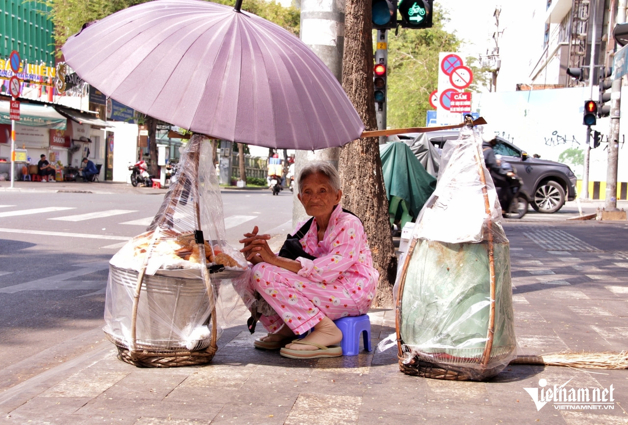 Cụ Hoa ngồi đợi người xe ôm thân quen đến chở mình đi bán bánh dạo tại các trung tâm thương mại khu vực phường Sài Gòn, TPHCM
