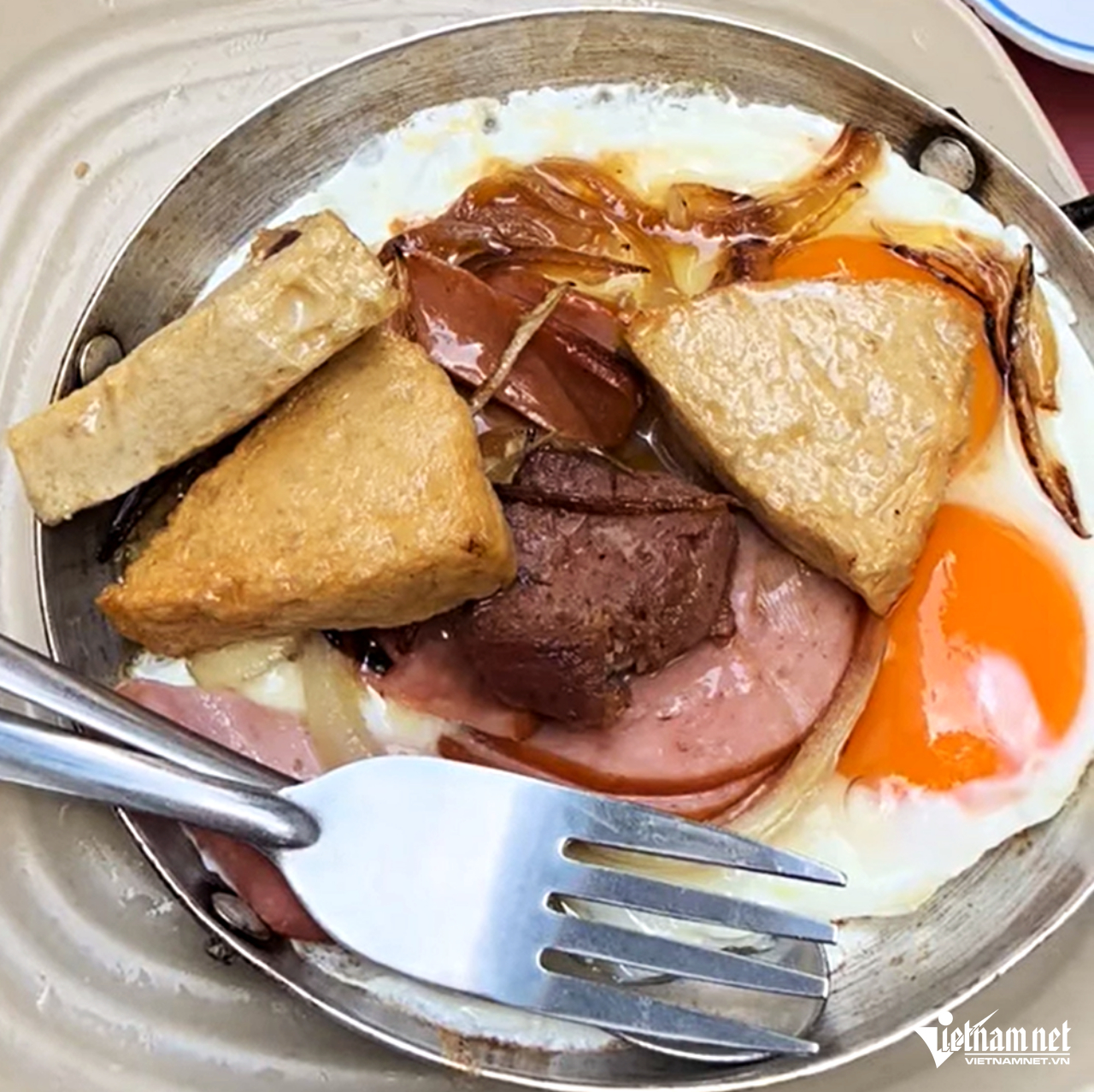 Món bánh mì ốp-la được chế biến trong chảo với trứng gà chiên, giăm bông, chả lụa, chả quế, xúc xích, thịt ba rọi muối...