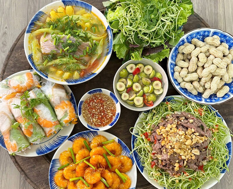 Mâm cơm này gồm các món: Tôm rang hành, nộm bò rau muống, canh cá nấu chua, bánh tráng cuốn tôm thịt, lạc luộc, sung muối.