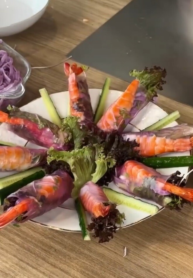 Đĩa gỏi cuốn tôm sắc tím hoàn thành xuất sắc và được cô bày biện cực kỳ nghệ thuật trên một chiếc đĩa lớn. Các chiếc gỏi cuốn được xếp quây tròn thành hình một bông hoa rực rỡ, trang trí xung quanh bằng những thanh dưa leo cắt khúc xanh mát.