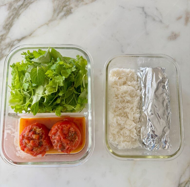 Hộp cơm bento chỉn chu gồm cà chua nhồi thịt sốt cà mặn mà cùng rau thơm sạch sẽ. Sự phân chia ngăn nắp giữa cơm trắng và thức ăn cho thấy tính cách tỉ mỉ, khoa học của cô trong việc chăm sóc sức khỏe con cái.