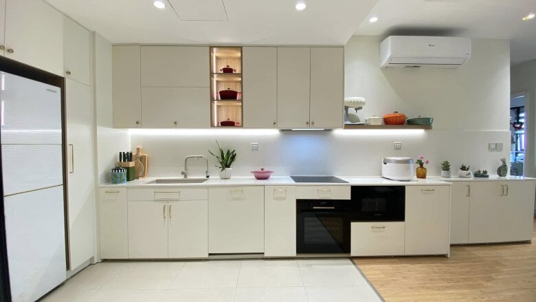 Hệ tủ bếp sáng màu kịch trần kết hợp với các ngăn kệ gỗ có đèn LED âm tủ, tối ưu diện tích lưu trữ và tạo cảm giác sang trọng.