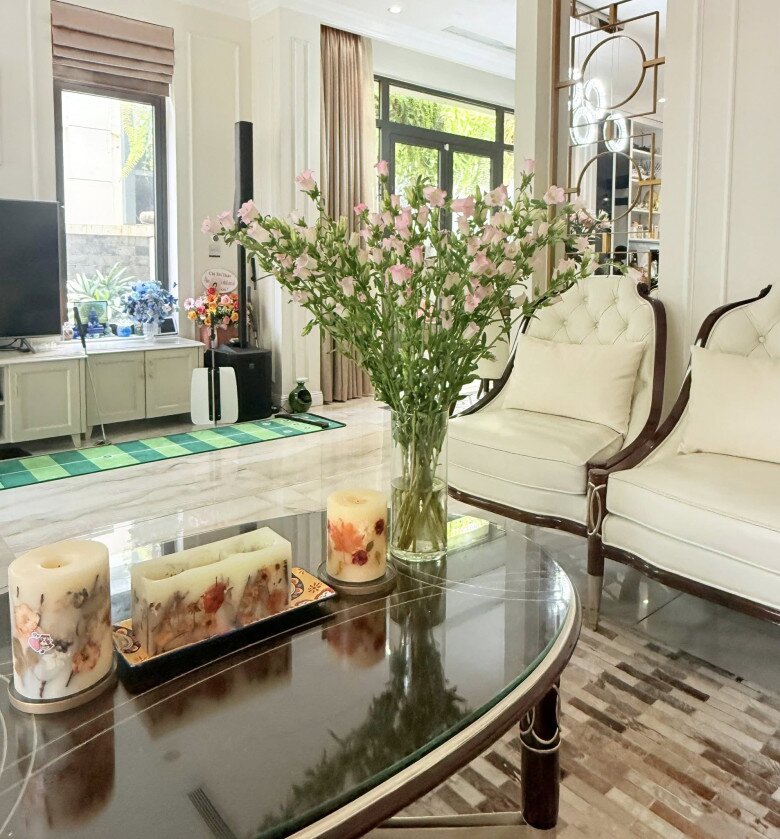 Tổng thể phòng khách rộng rãi, hiện đại nhà nữ MC với bình hoa chuông tán rộng đặt tại vị trí trung tâm trên bàn trà. Cách bài trí này kết hợp hài hòa với các bộ nến thơm nghệ thuật, tạo nên không gian đón khách ấm cúng.