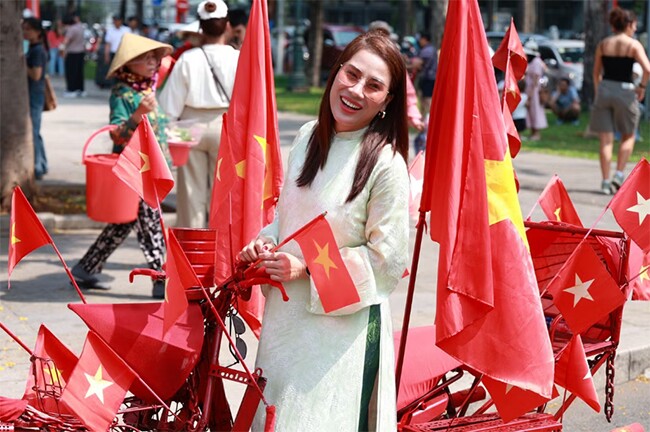 Người phụ nữ chụp ảnh bên chiếc xe trang hoàng nhiều lá cờ đỏ sao vàng.