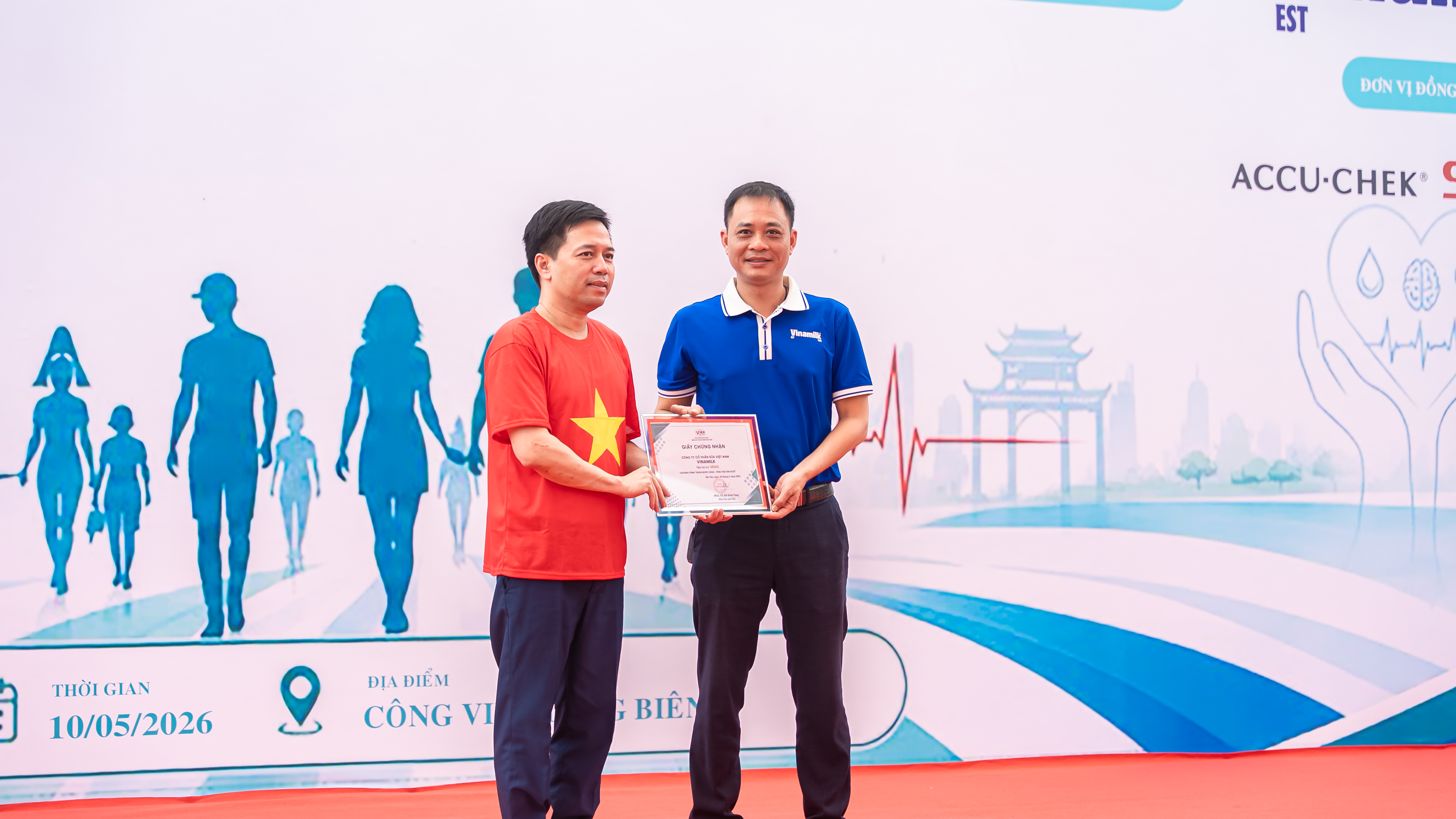 Ông Vũ Tuấn Khang (áo xanh) - Giám đốc Kinh doanh Hà Nội, Công ty Cổ phần sữa Việt Nam (Vinamilk) – nhận chứng nhận tài trợ từ Ban tổ chức chương trình “Ngàn bước chân – Triệu trái tim khỏe”