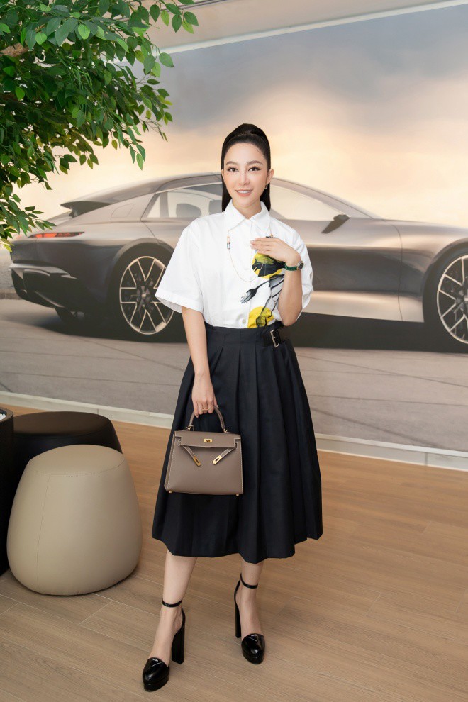 Cô diện chân váy đen kết hợp áo sơ mi trắng in họa tiết, xách túi hiệu xa xỉ.