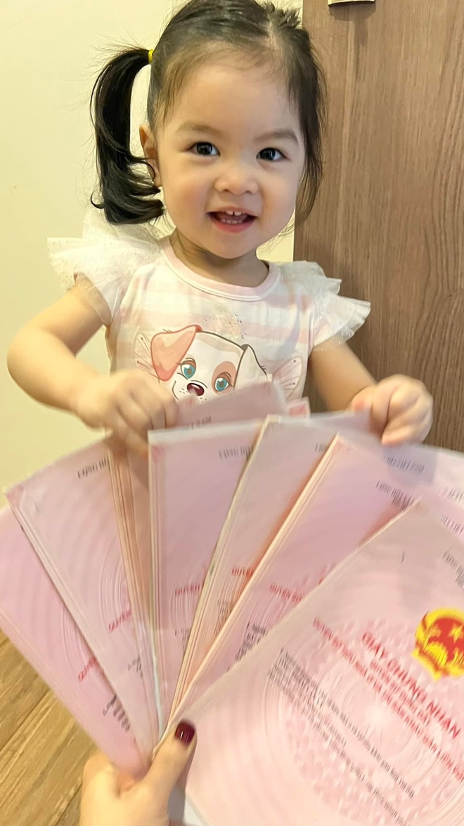 Con gái thứ 2 của Trần Bảo Sơn dễ thương, xinh xắn, đang cầm sấp sổ đỏ trên tay.