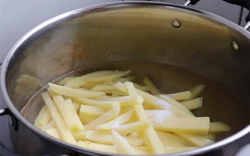 Bước tiếp theo vô cùng quan trọng, là một trong những yếu tố giúp khoai không bị ỉu sau khi chiên, đó là chần khoai. Đun sôi nước, cho khoai tây vào chần khoảng 2 phút, cho vào nồi một thìa muối để khoai tây thơm ngon hơn.
