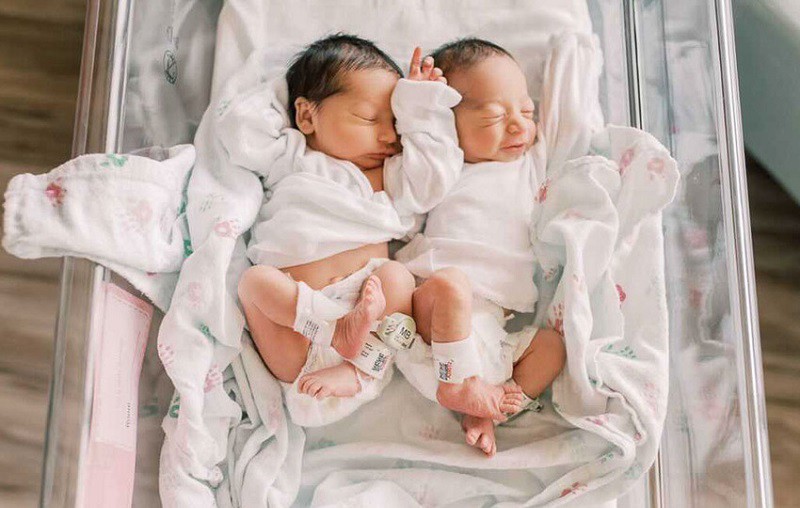 Hai bé sinh đôi tạo dáng y hệt nhau khi nằm trong chiếc nôi.
