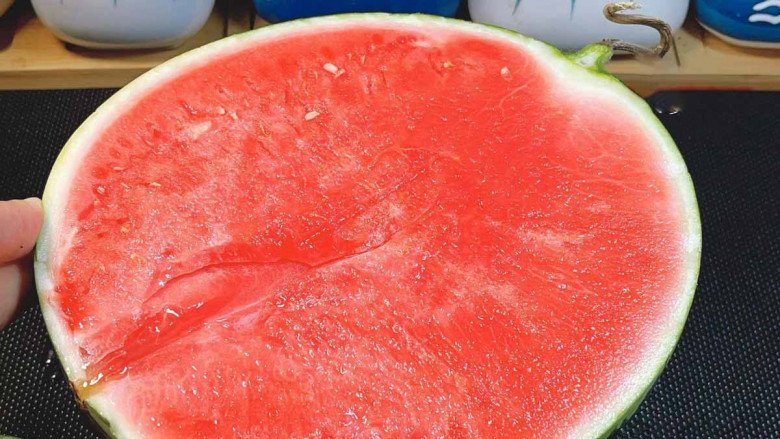 A hand holding a chopstick, about to pierce a watermelon