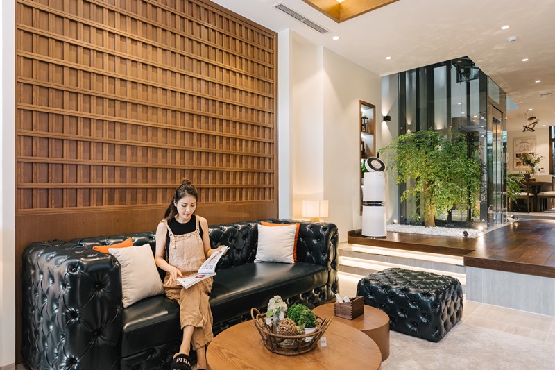 Phòng khách được đặt một bộ sofa màu đen sang trọng kết hợp với bàn gỗ. Khu vực ăn uống, nấu nướng được nâng cao hơn, kết nối với phòng khách bằng bậc thang ngắn.
