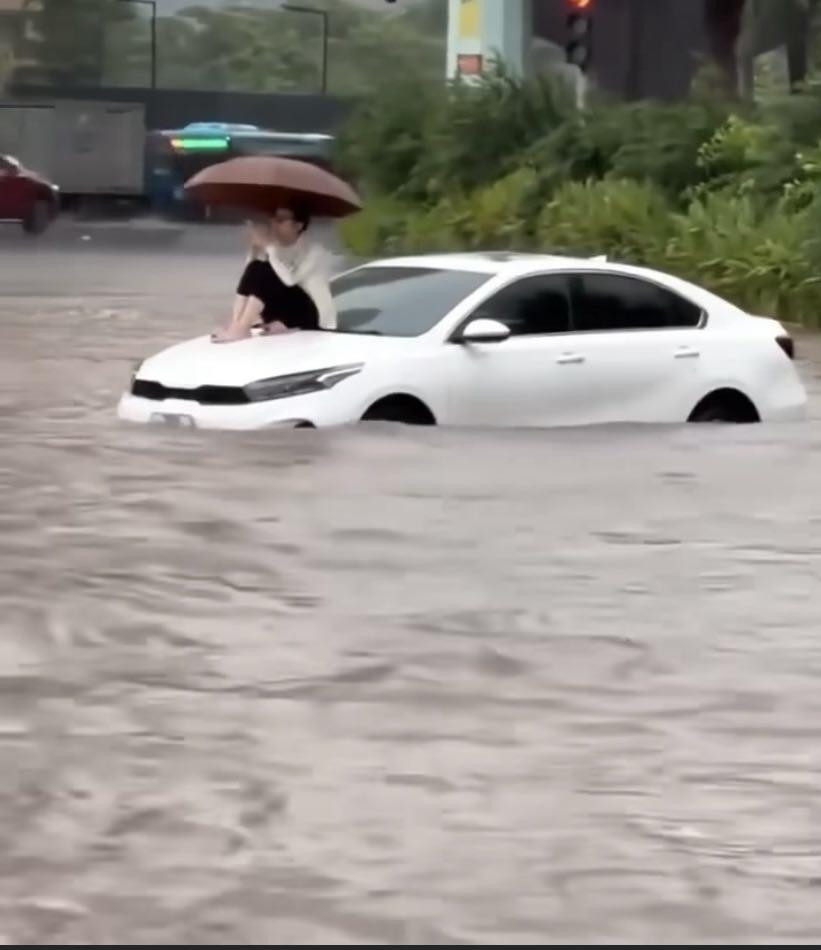 Chị C. cầm ô ngồi trên nắp capo giữa mệnh mông “biển nước” gây sốt mạng.