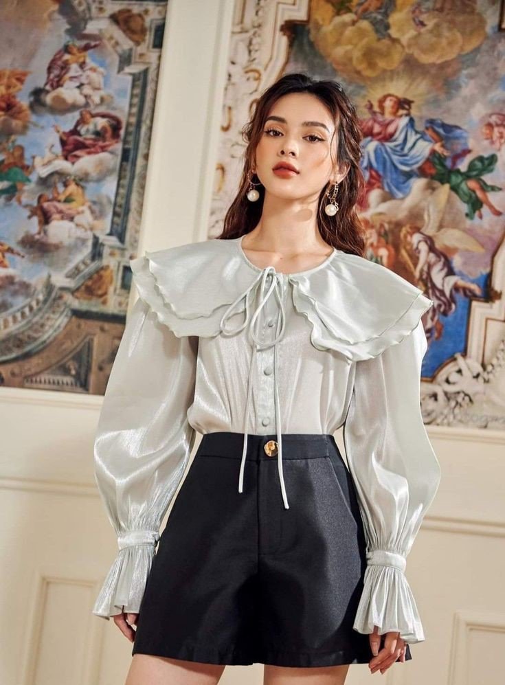 Outfit phù hợp cho những ngày đi làm nhưng trời mưa là áo blouse tay bồng cổ bèo và quần short hoặc chân váy ngắn chữ A. Sự kết hợp này vừa năng động vừa cá tính, giúp chị em dễ dàng di chuyển trong những ngày mưa nhưng vẫn giữ được sự trẻ trung duyên dáng.