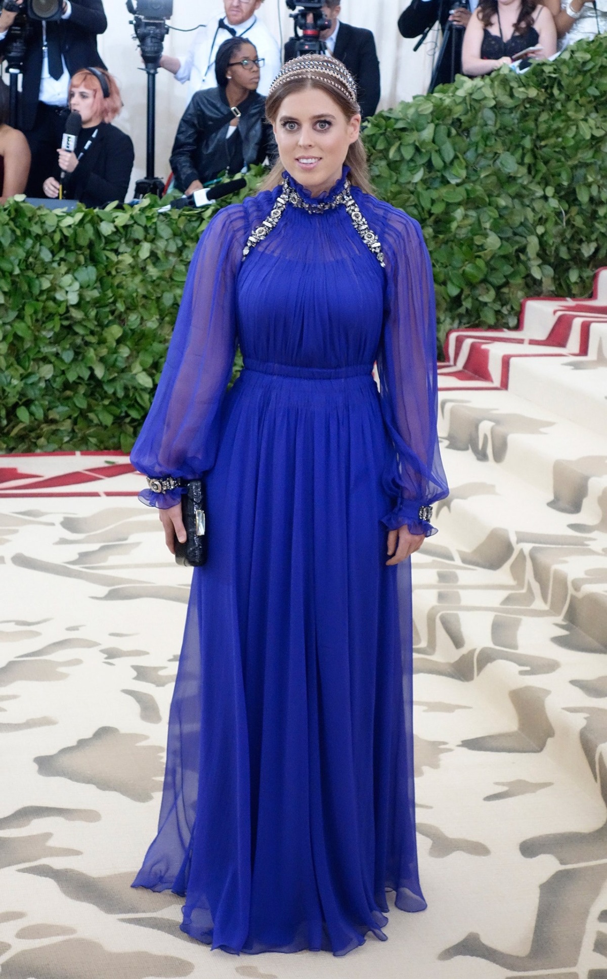 Công chúa Beatrice dự Met Gala 2018. Vogue nhận xét phong cách của cô đơn giản nhưng vẫn bắt mắt nhờ bộ đầm cao cổ bằng lụa chiffon màu xanh navy của Alberta Ferretti, điểm chi tiết đính đá ở cổ và gấu tay. Chiếc băng đô đính đá và son màu nude khiến vẻ ngoài của cô trở nên hoàn hảo.